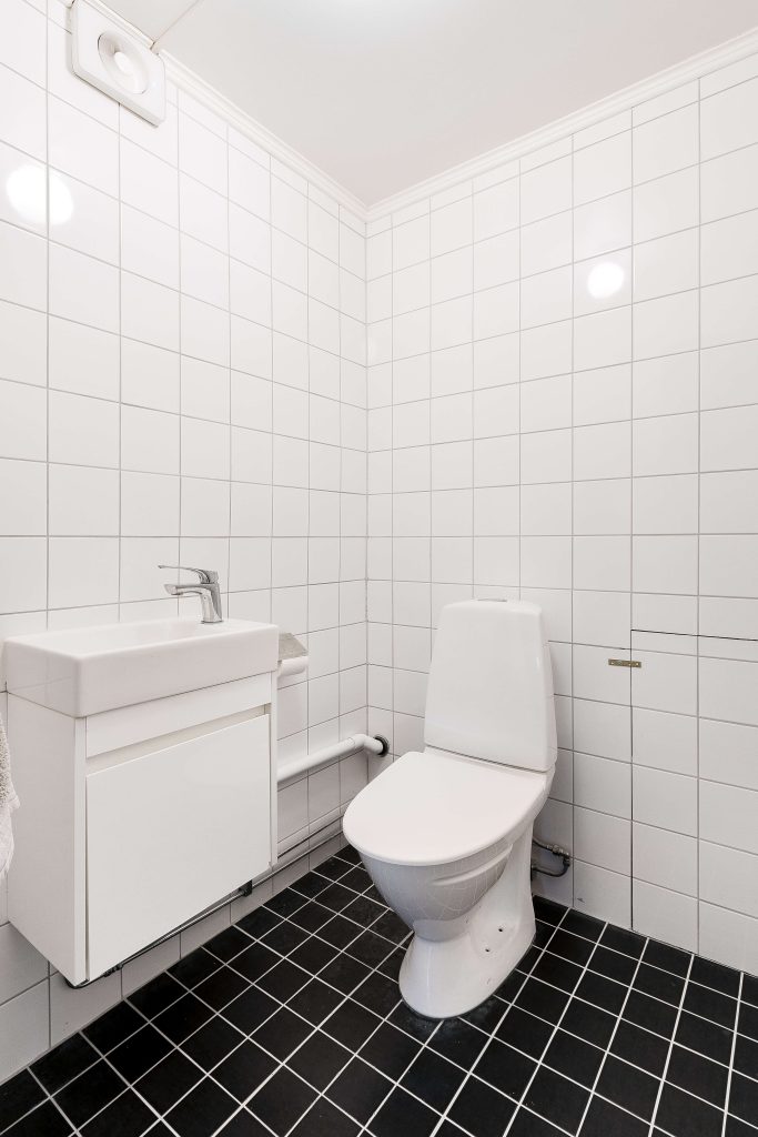 Toalett och handfat i vitkaklat badrum.