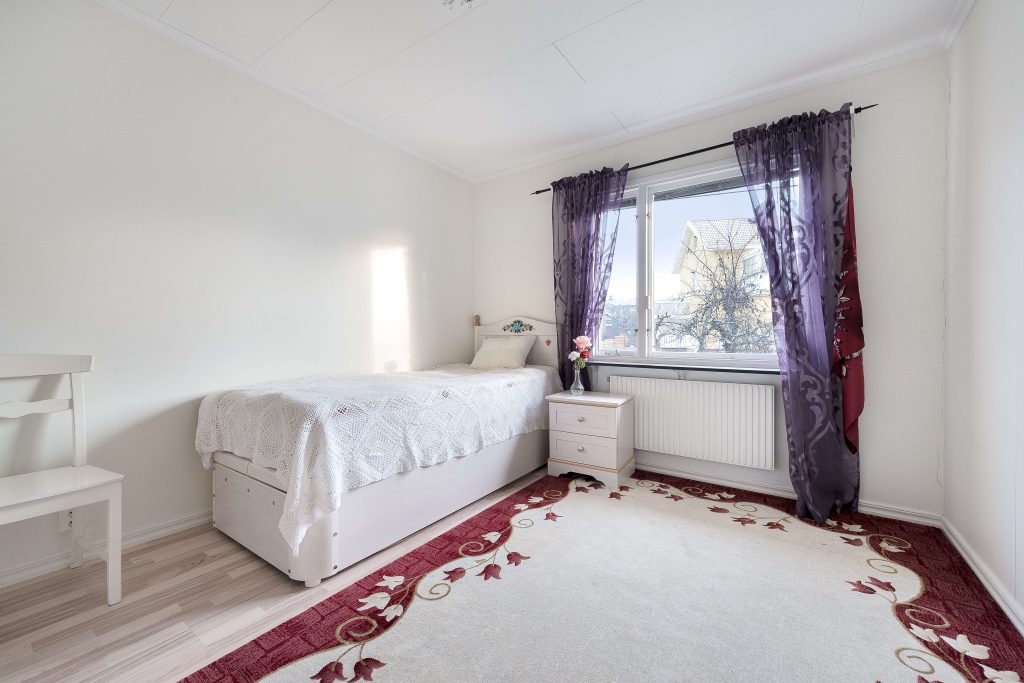 Sovrum med enkelsäng och lila gardiner.