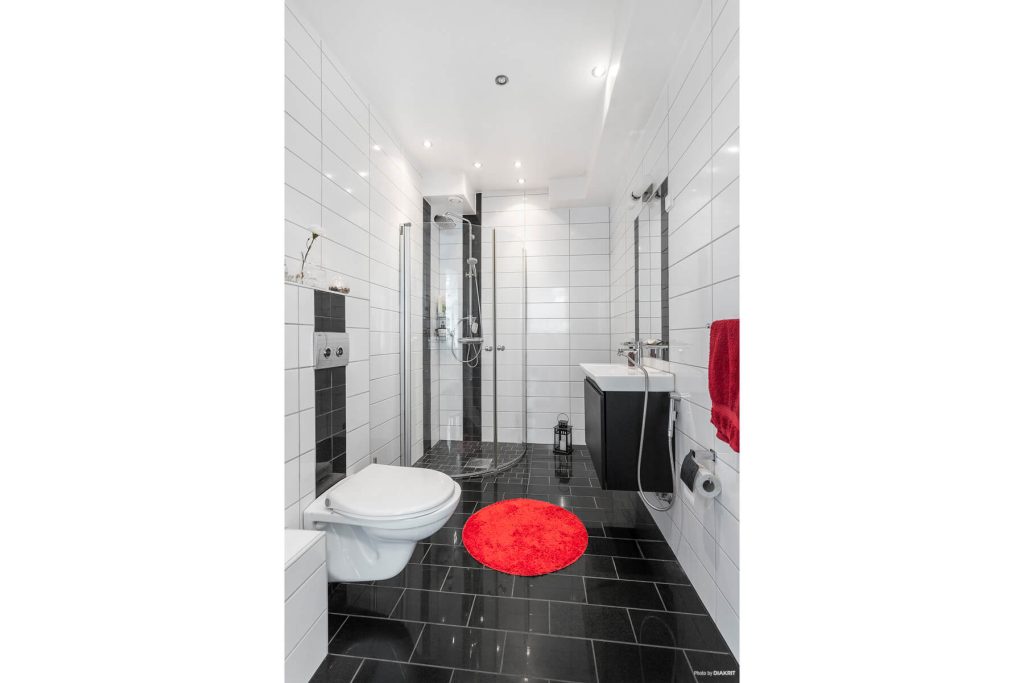 Badrum med svart golv och röd rund badrumsmatta.